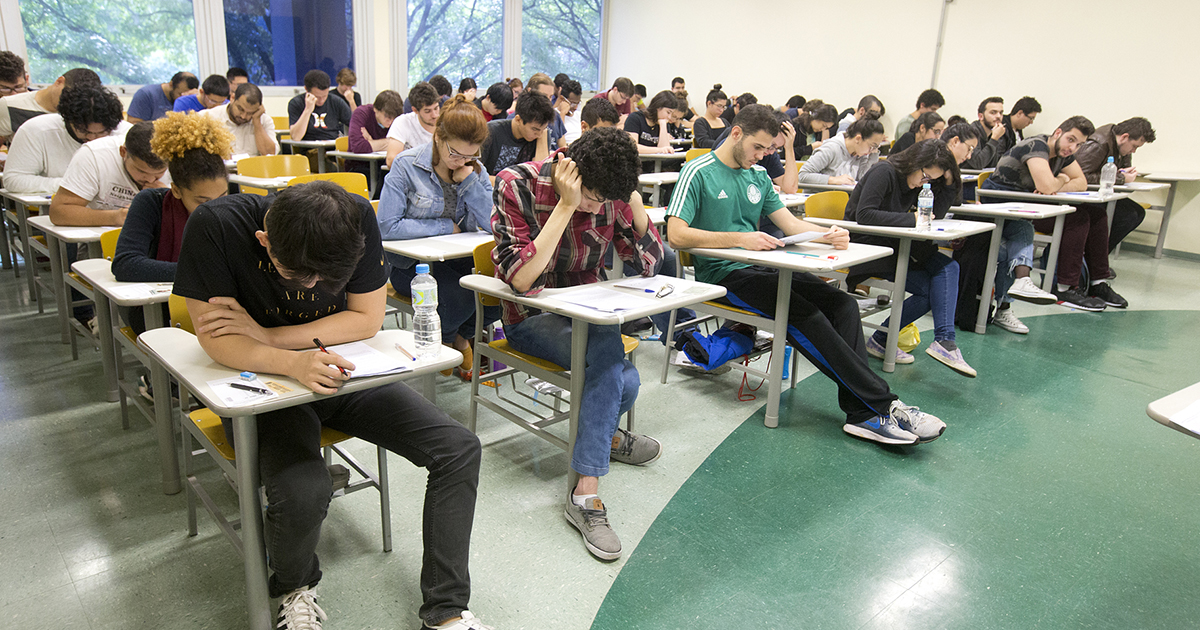 Imagem ilustrativa de candidatos sentados em carteiras enfileiradas, resolvendo questões em sala de aula, em referência à primeira fase da Fuvest 2027