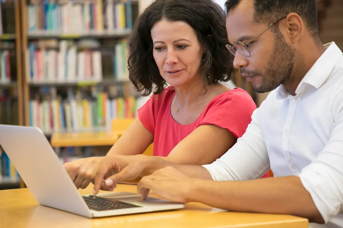 Professores da educação básica utilizam notebook em biblioteca para representar cursos gratuitos de pós-graduação.