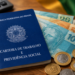 Carteira de Trabalho azul sobre mesa com notas e moedas de real próximas a caneta e bandeira do Brasil, simbolizando as novas profissões que podem receber o adicional de 40%.