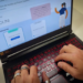 Mãos de pessoa digitando em notebook, tela exibe Portal Prouni gov.br, simbolizando a lista de espera do Prouni.