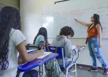 Professora aplicando aula em sala de ensino com alunos durante atividade escolar.