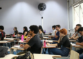 Estudantes sentados em carteiras de uma sala de aula, com cadernos e garrafas de água sobre as mesas, acompanhando a aula durante a preparação para o Provão Paulista.
