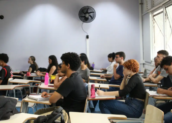 Estudantes sentados em carteiras de uma sala de aula, com cadernos e garrafas de água sobre as mesas, acompanhando a aula durante a preparação para o Provão Paulista.