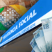 Placa do INSS com dinheiro, notas de 100, 50 e 20 reais em destaque e logomarca colorida ao centro, simbolizando o reajuste do salário mínimo em 2027 que poderá impactar os pagamentos do INSS.