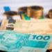 Cédulas de dinheiro brasileiro e moedas representam as diferenças entre salário mínimo, piso salarial e salário normativo.