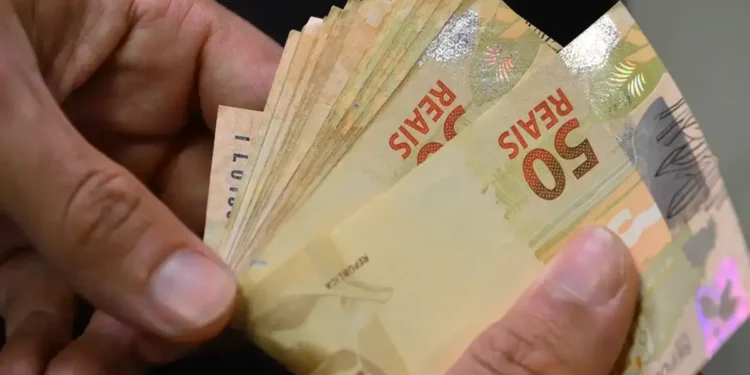 Mãos masculinas segurando várias notas de R$ 50 reais brasileiras em leque, simbolizando o ressarcimento PIS/Pasep.