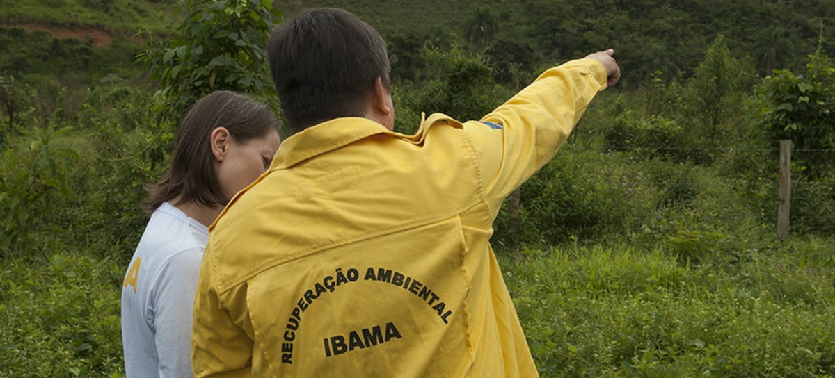 Servidor com jaqueta de recuperação ambiental do Ibama apontando para área de vegetação em campo