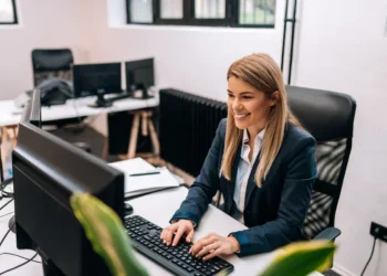 Profissional de secretariado trabalhando em computador em ambiente de escritório.