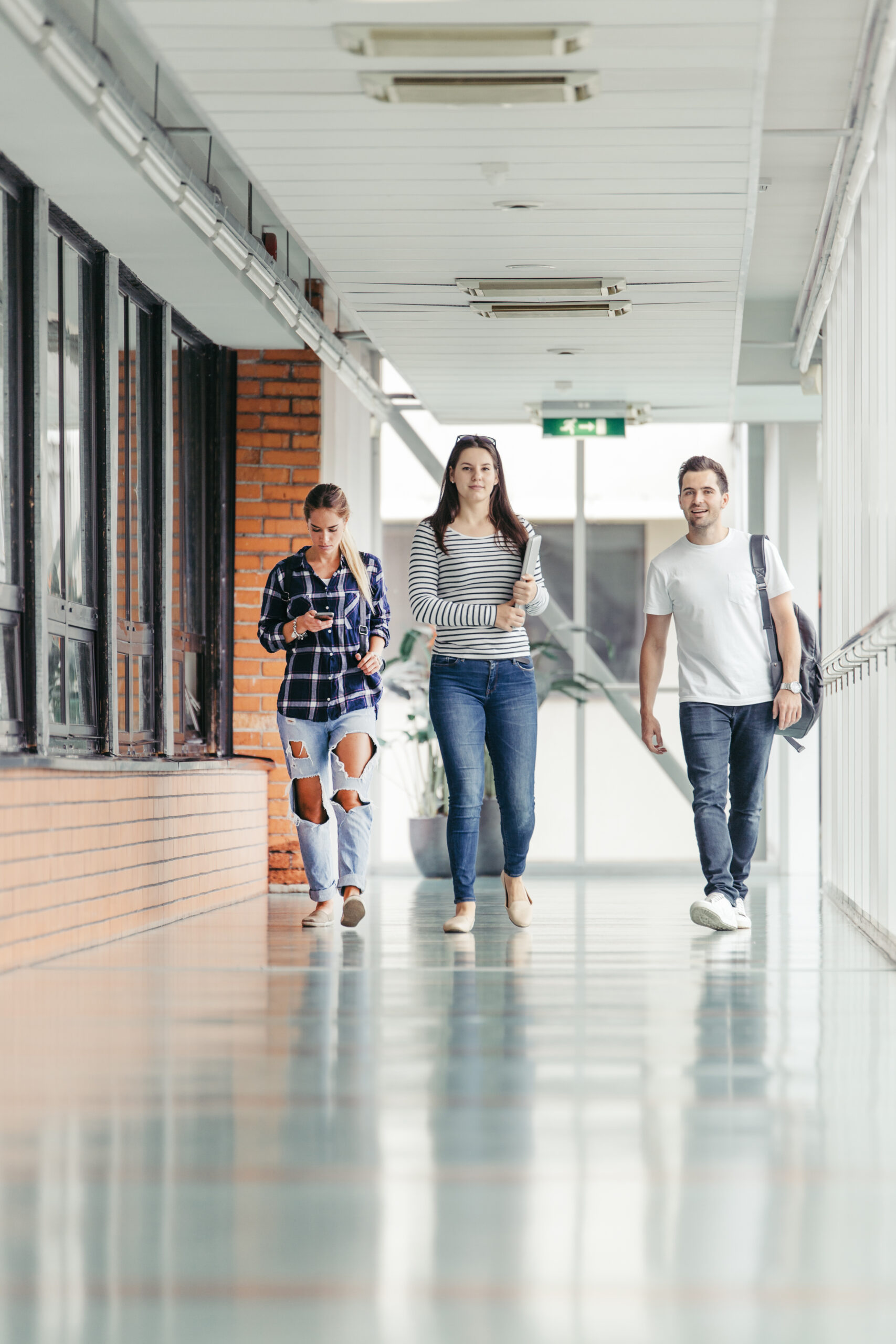 Três jovens adultos caminhando em corredor de universidade: duas mulheres e um homem com roupas casuais, simbolizando o horário de aplicação da PND 2026.