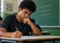 Estudante escrevendo a redação do Enem em sala de aula, representando a possível troca do modelo tradicional por textos mais curtos.