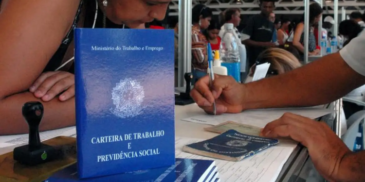 Candidata em balcão de atendimento de um mutirão de emprego com atendente preenchendo formulários, ao lado de exemplares da Carteira de Trabalho e Previdência Social.