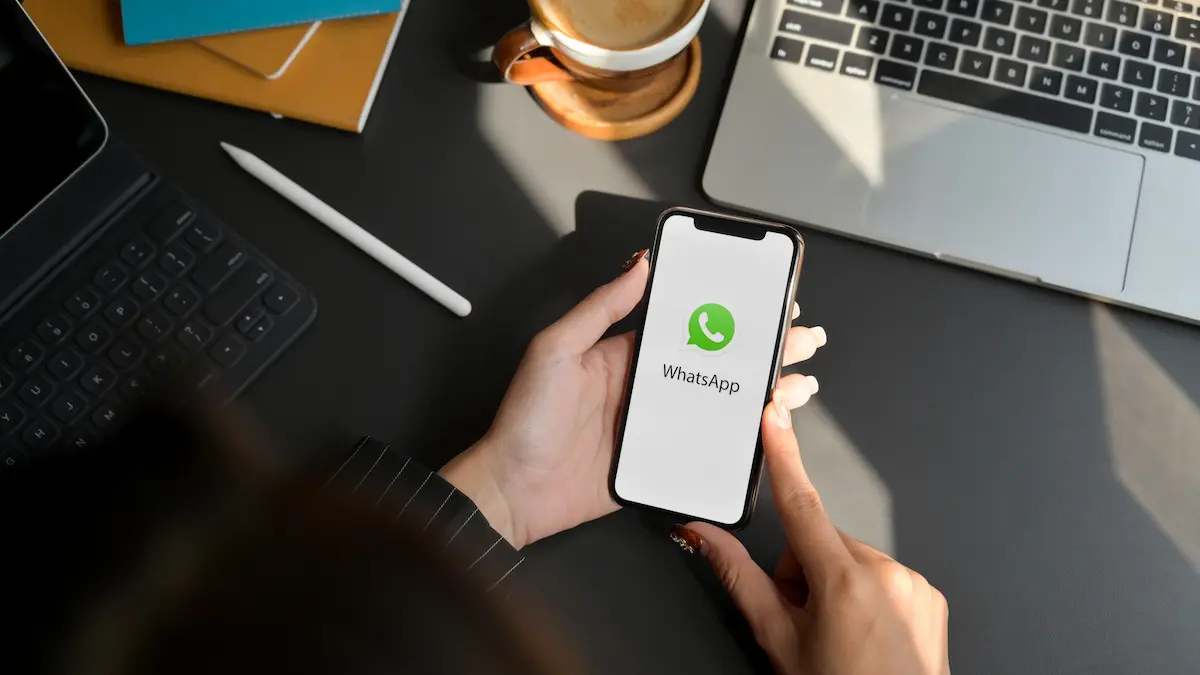 Usuário segura celular com WhatsApp aberto representando a escolha de manter ou desativar a transcrição de áudios no aplicativo.