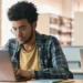 Jovem estudando em biblioteca universitária usando notebook.