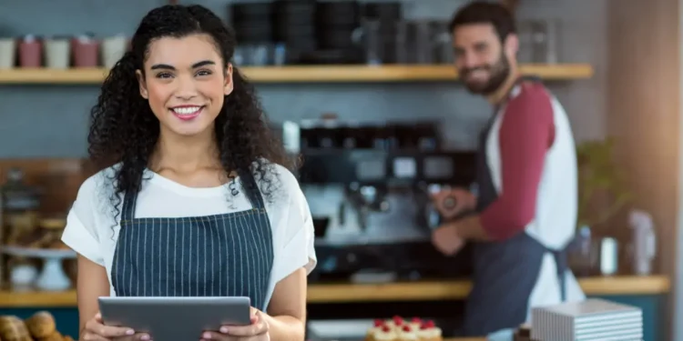 Barista sorridente com tablet em cafeteria moderna.