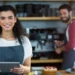 Barista sorridente com tablet em cafeteria moderna.