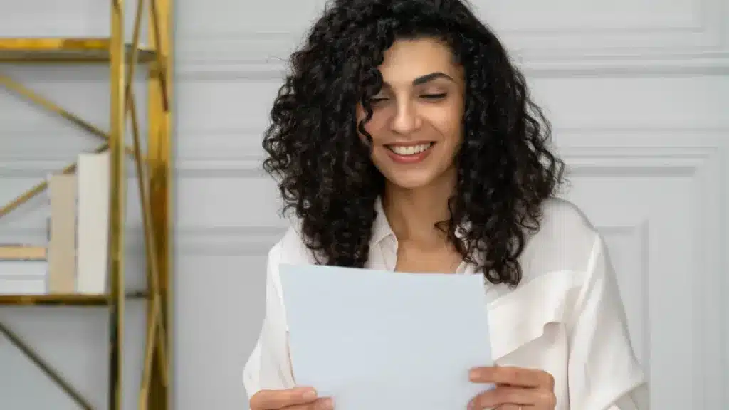 Jovem mulher sorrindo ao ler carta em ambiente sofisticado.