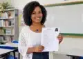 Professora sorrindo e segurando seu currículo em uma sala de aula.