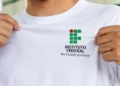 Mãos masculinas seguram uma camiseta branca com o logotipo do IFRN em destaque.