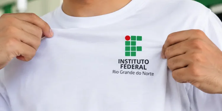 Mãos masculinas seguram uma camiseta branca com o logotipo do IFRN em destaque.