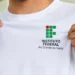 Mãos masculinas seguram uma camiseta branca com o logotipo do IFRN em destaque.