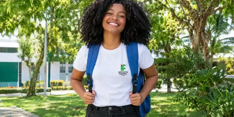 Estudante negra sorrindo, com mochila azul e camiseta do IFS, em um campus arborizado.