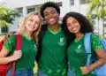 Três estudantes do Ifac sorrindo e abraçados em frente ao campus.