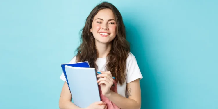 Estudante jovem sorridente com cadernos em fundo azul.