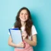 Estudante jovem sorridente com cadernos em fundo azul.