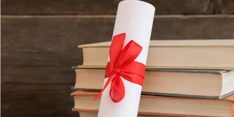 Diploma enrolado com fita vermelha ao lado de livros empilhados.