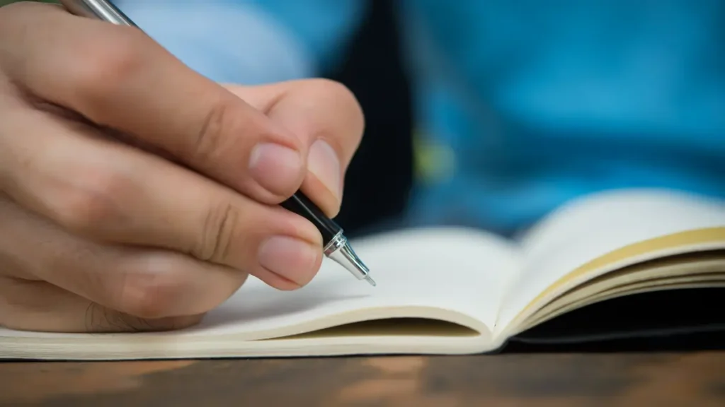 Pessoa escrevendo em caderno aberto com caneta preta.