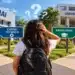 Jovem de mochila observa placas “Curso Técnico” e “Faculdade” diante do SENAI e universidade federal, simbolizando a dúvida entre cursos técnicos e faculdade.