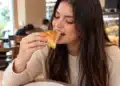 Mulher comendo esfirra em padaria aconchegante.