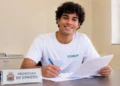 Jovem estagiário sorrindo com documentos na Prefeitura de Vinhedo.