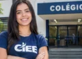 Jovem sorrindo com camiseta do CIEE em frente a uma escola.