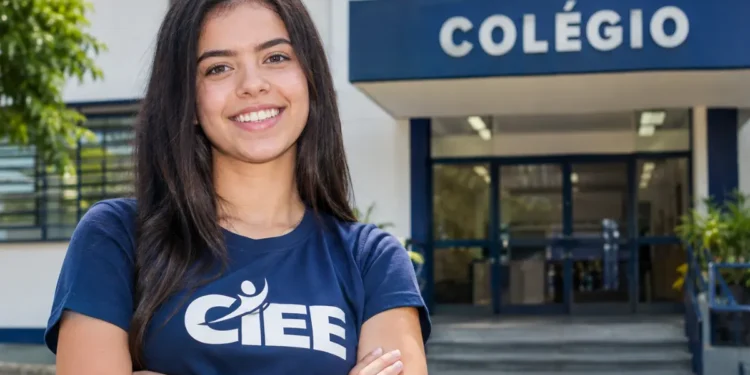 Jovem sorrindo com camiseta do CIEE em frente a uma escola.