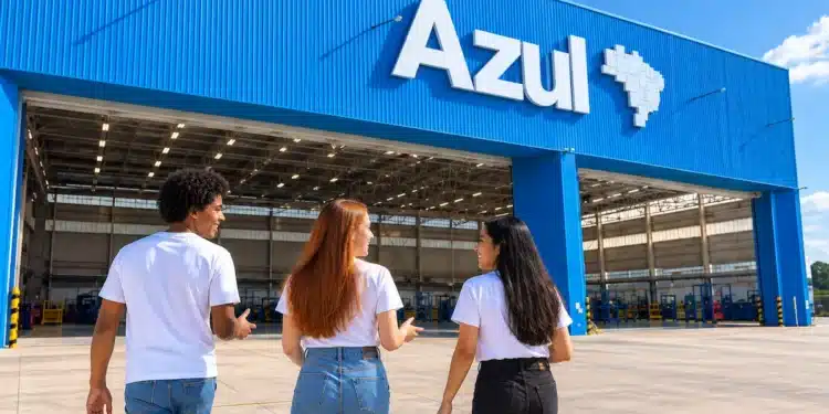 Três jovens conversam em frente ao hangar da Azul em um dia ensolarado.