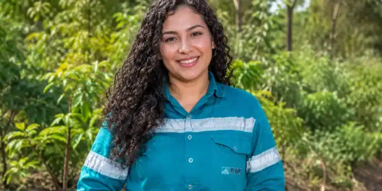 Jovem sorrindo com uniforme azul em uma área verde.