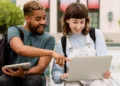 Jovens interagindo animados com notebook em área externa universitária.