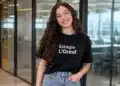 Jovem sorridente com camiseta de estágio da L’Oréal em ambiente corporativo.