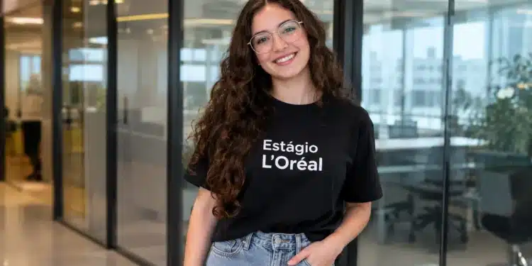 Jovem sorridente com camiseta de estágio da L’Oréal em ambiente corporativo.