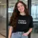 Jovem sorridente com camiseta de estágio da L’Oréal em ambiente corporativo.