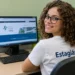 Estagiária sorrindo em escritório, com computador exibindo o site do TRF2 ao fundo.