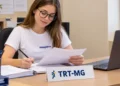 Jovem estagiária trabalha com documentos em uma mesa no TRT-MG.