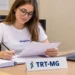 Jovem estagiária trabalha com documentos em uma mesa no TRT-MG.