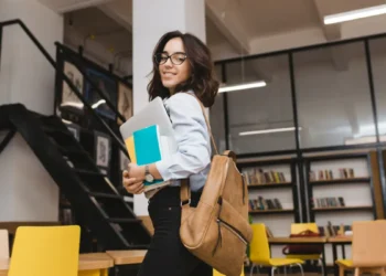 Jovem estudante sorridente com mochila em biblioteca moderna.