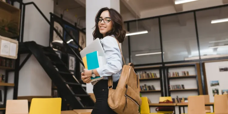 Jovem estudante sorridente com mochila em biblioteca moderna.