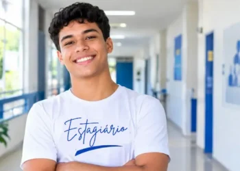 Jovem estagiário sorridente destaca-se em corredor institucional.