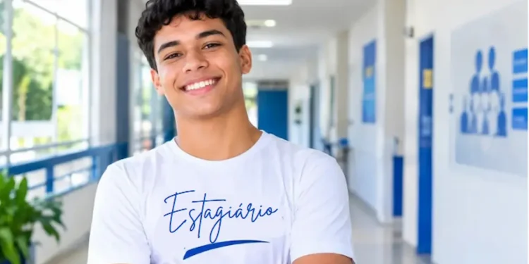 Jovem estagiário sorridente destaca-se em corredor institucional.