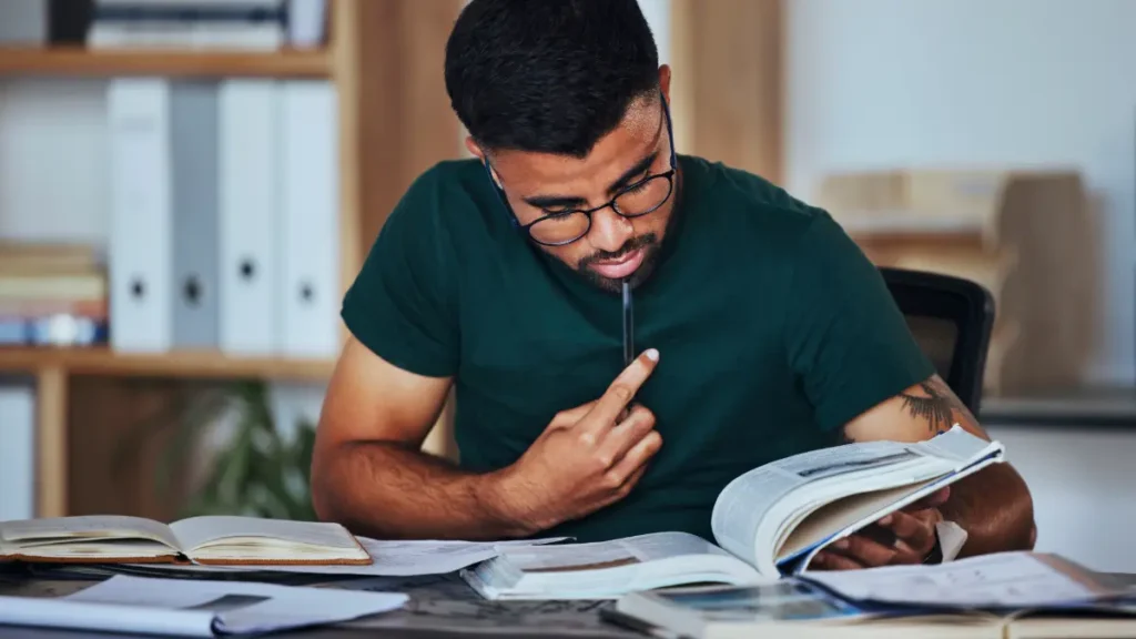 Jovem estudando concentrado com livros em mesa de escritório.