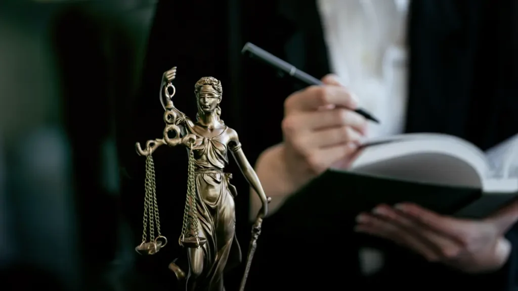 Justiça representada por estátua de deusa e pessoa escrevendo em caderno.